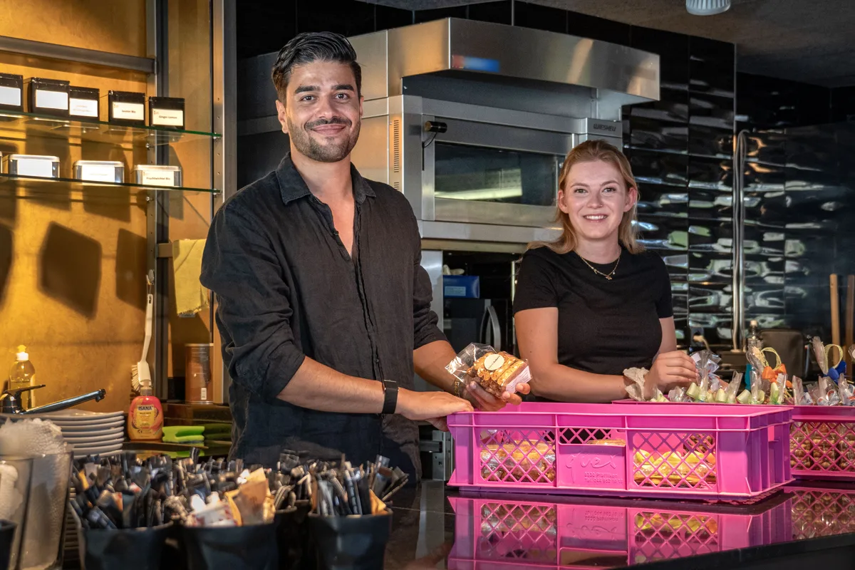 Ein Mann und eine Frau stehen hinter rosafarbenen Boxen mit Backwaren.